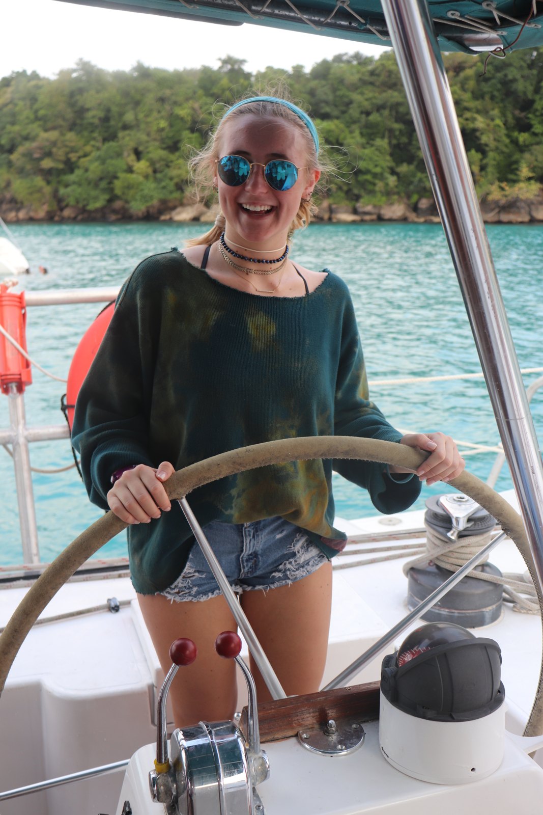 Katie smiling at the wheel of a boat, with blue water behind her